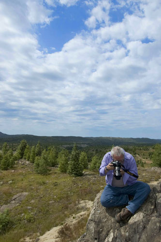 Photographer sitting on a rock with a forest and sky behind them.