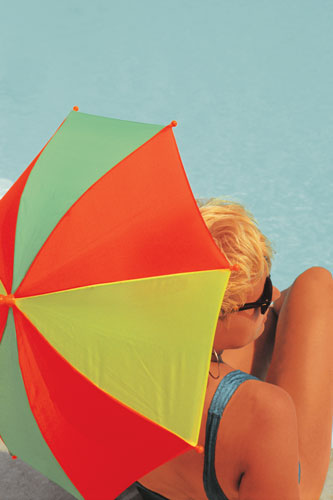 Woman with an umbrella sitting at a pool.