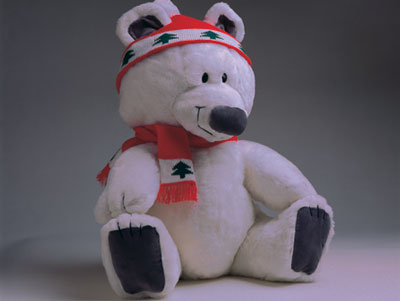 A white teddy bear wearing a red hat and scarf with pictures of trees on it.
